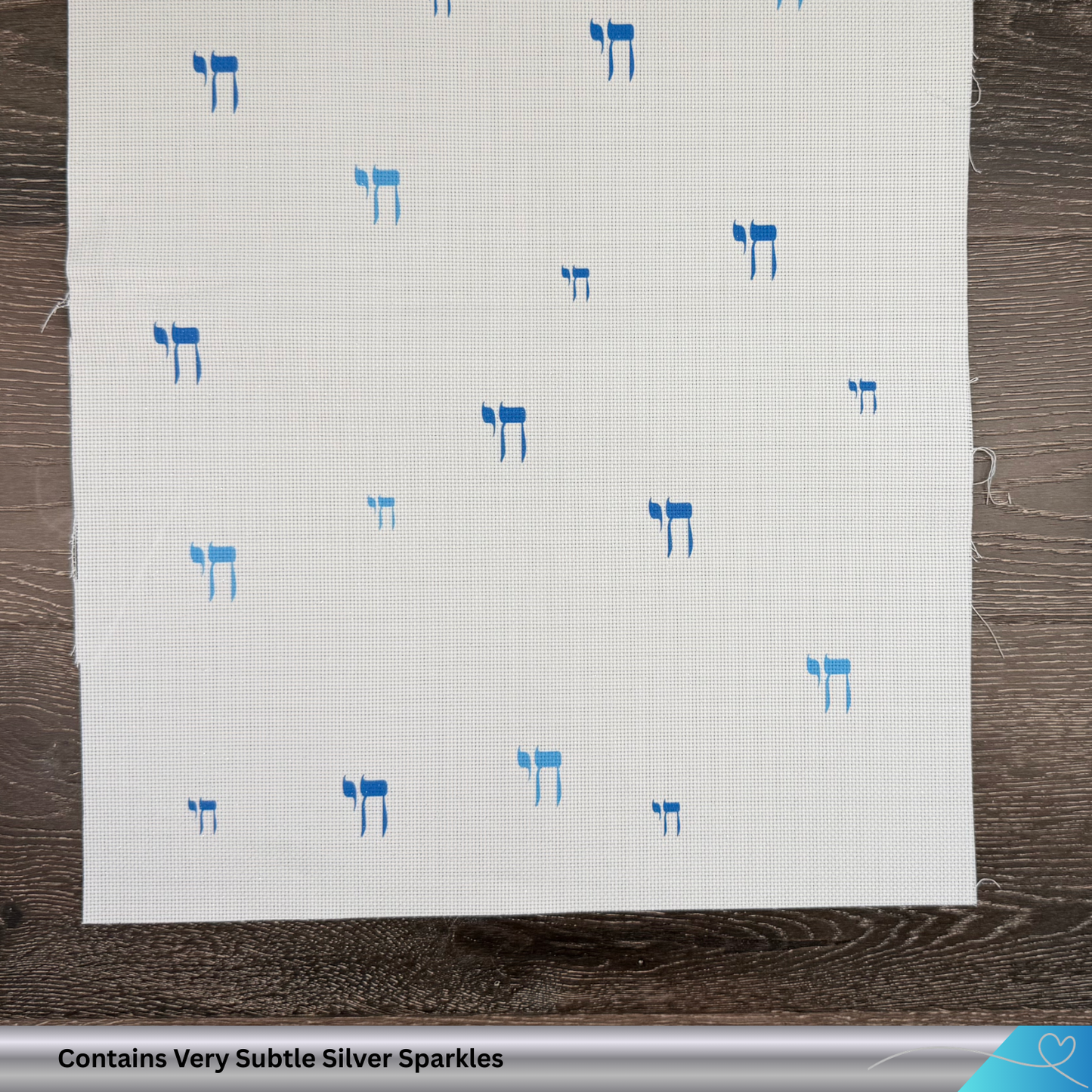 White fabric with blue Hebrew text patterns on a wooden surface. Contains hints of silver glitter.