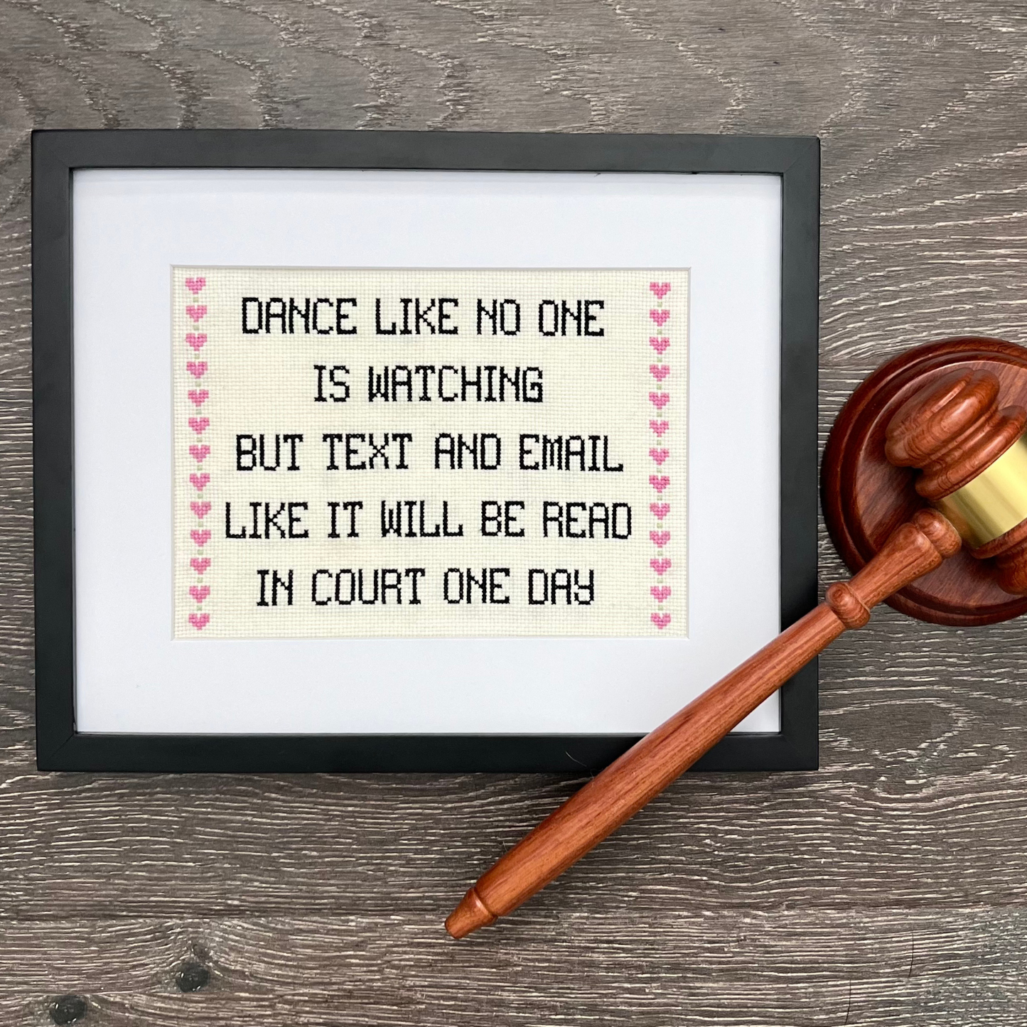 Framed cross-stitched quote with a gavel on a wooden surface