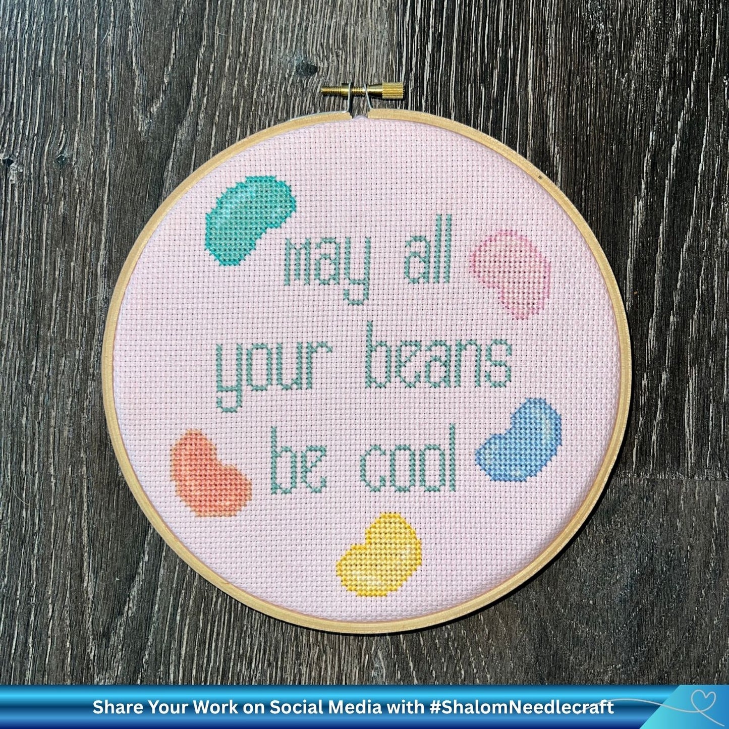 Embroidery hoop with cross-stitched text and colorful beans on a wooden surface