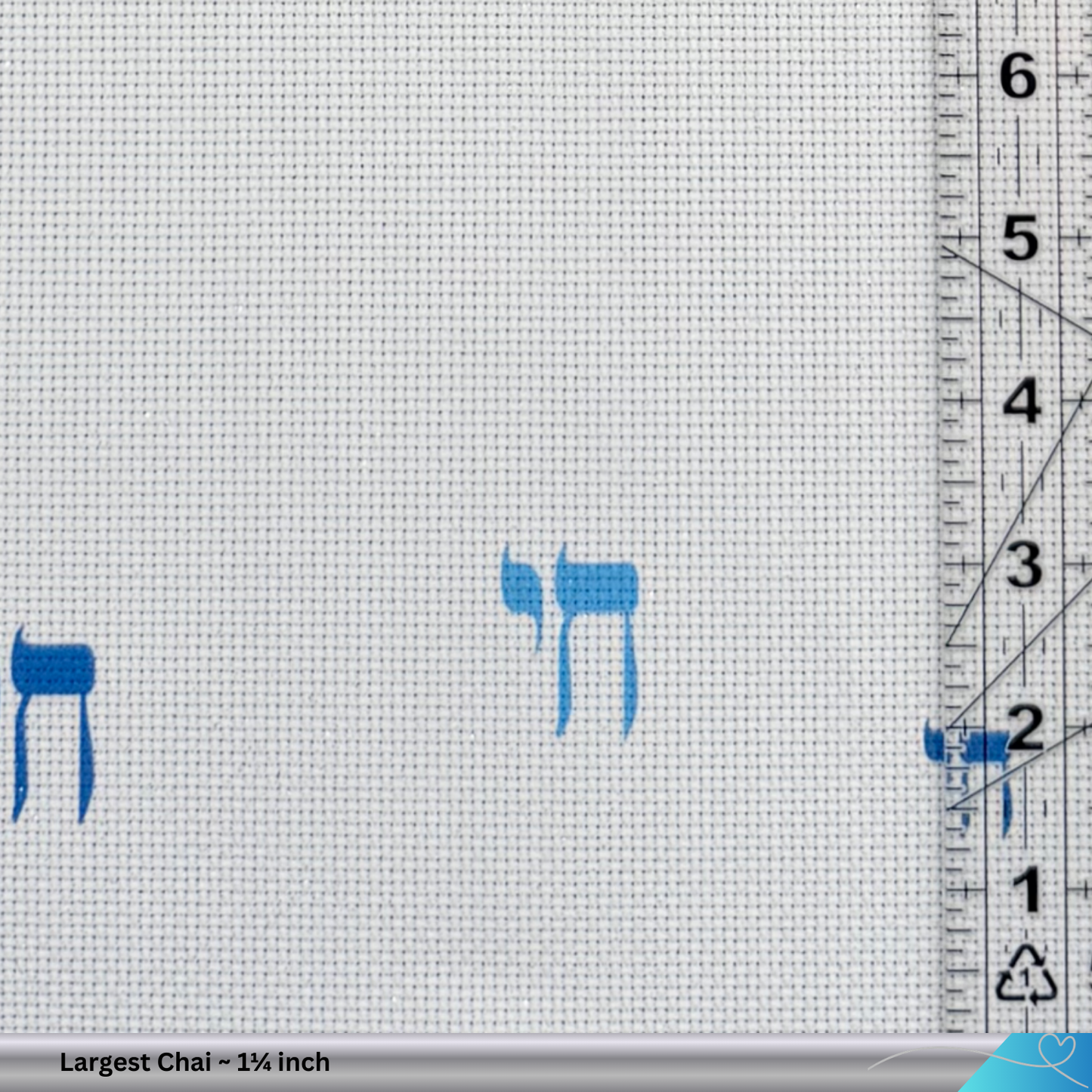 Cross-stitch pattern with blue 'Chai' symbols on white fabric, ruler for scale.