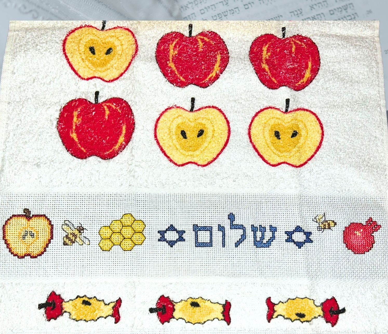 Cross-stitched design with apples, honey, and the Hebrew word 'Shalom' on a hand towel.