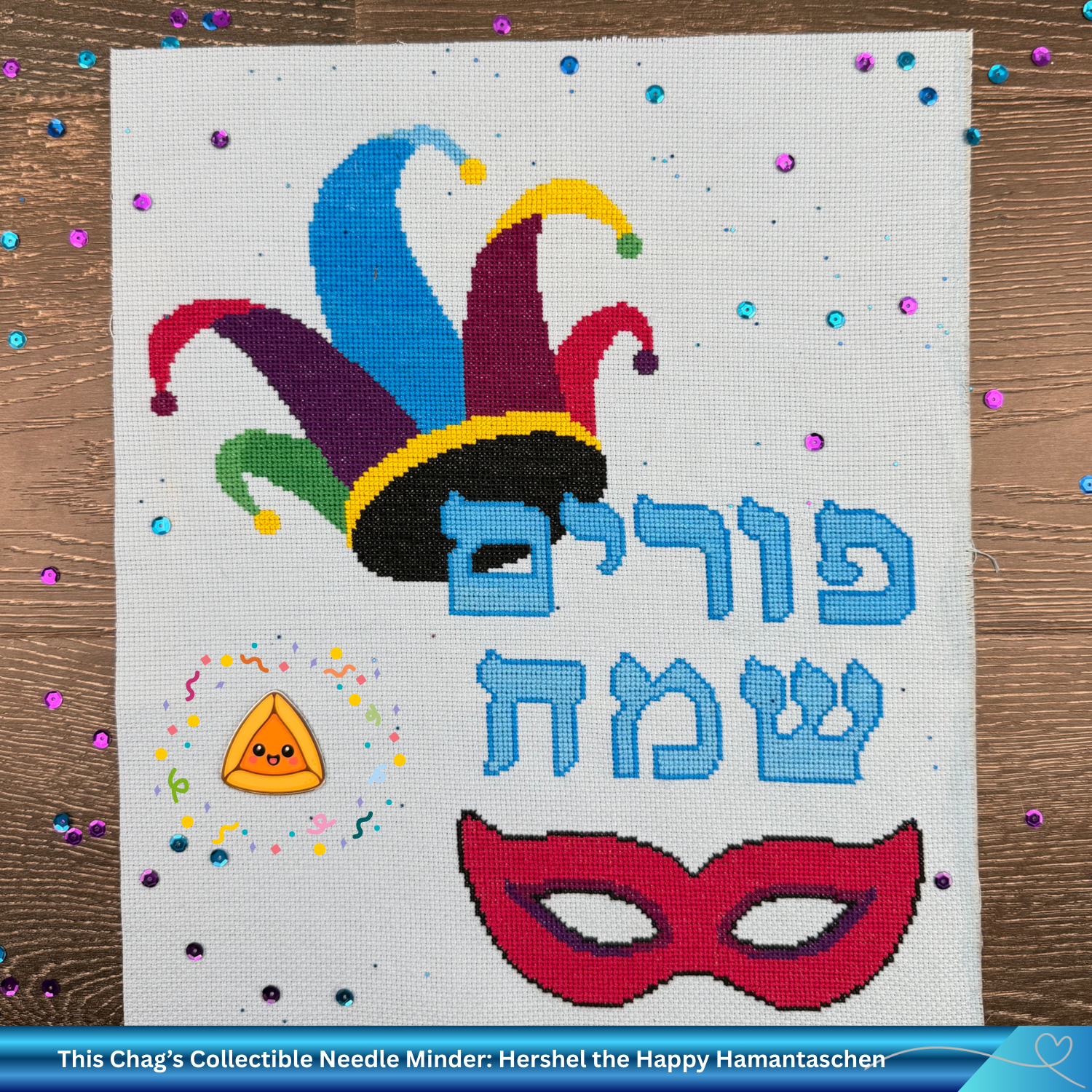 Cross-stitched design with a colorful jester hat, mask, and Hebrew text on a wooden surface with confetti.