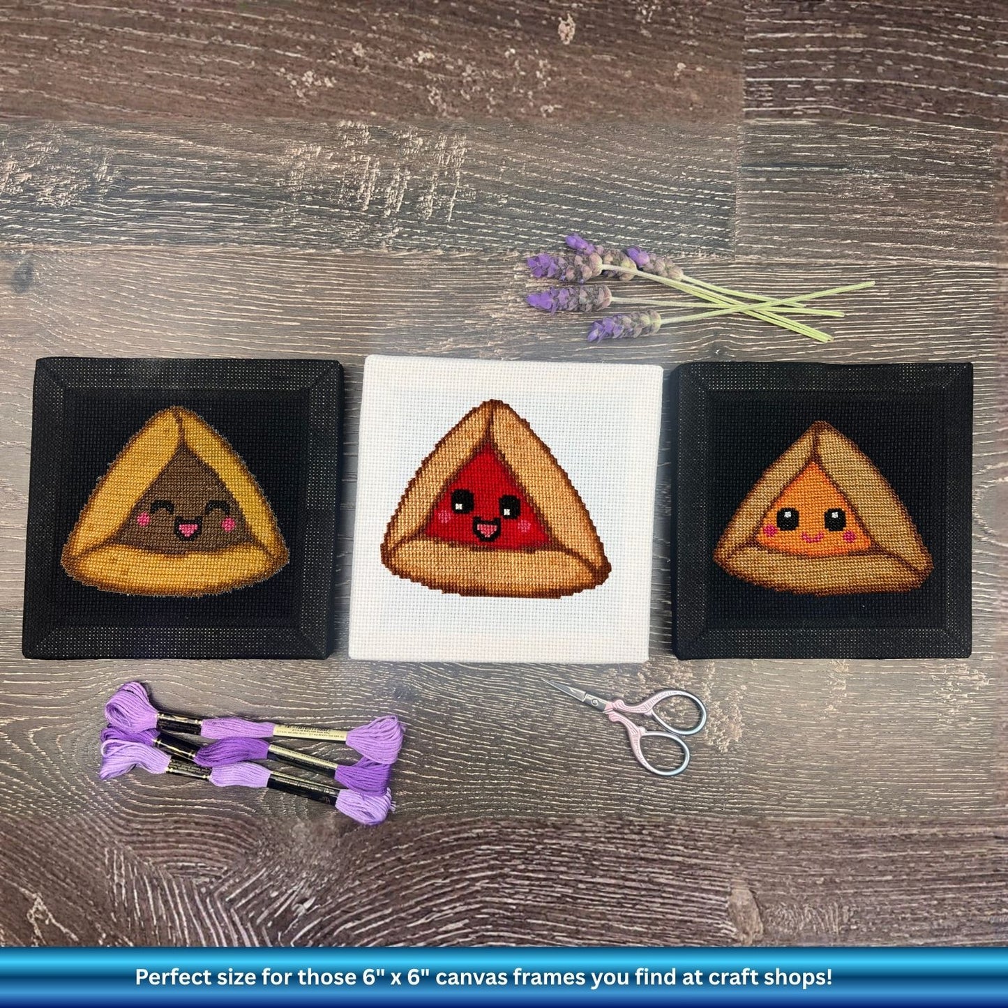 Three embroidered triangular hamantaschen with faces on a wooden surface with scissors and lavender.