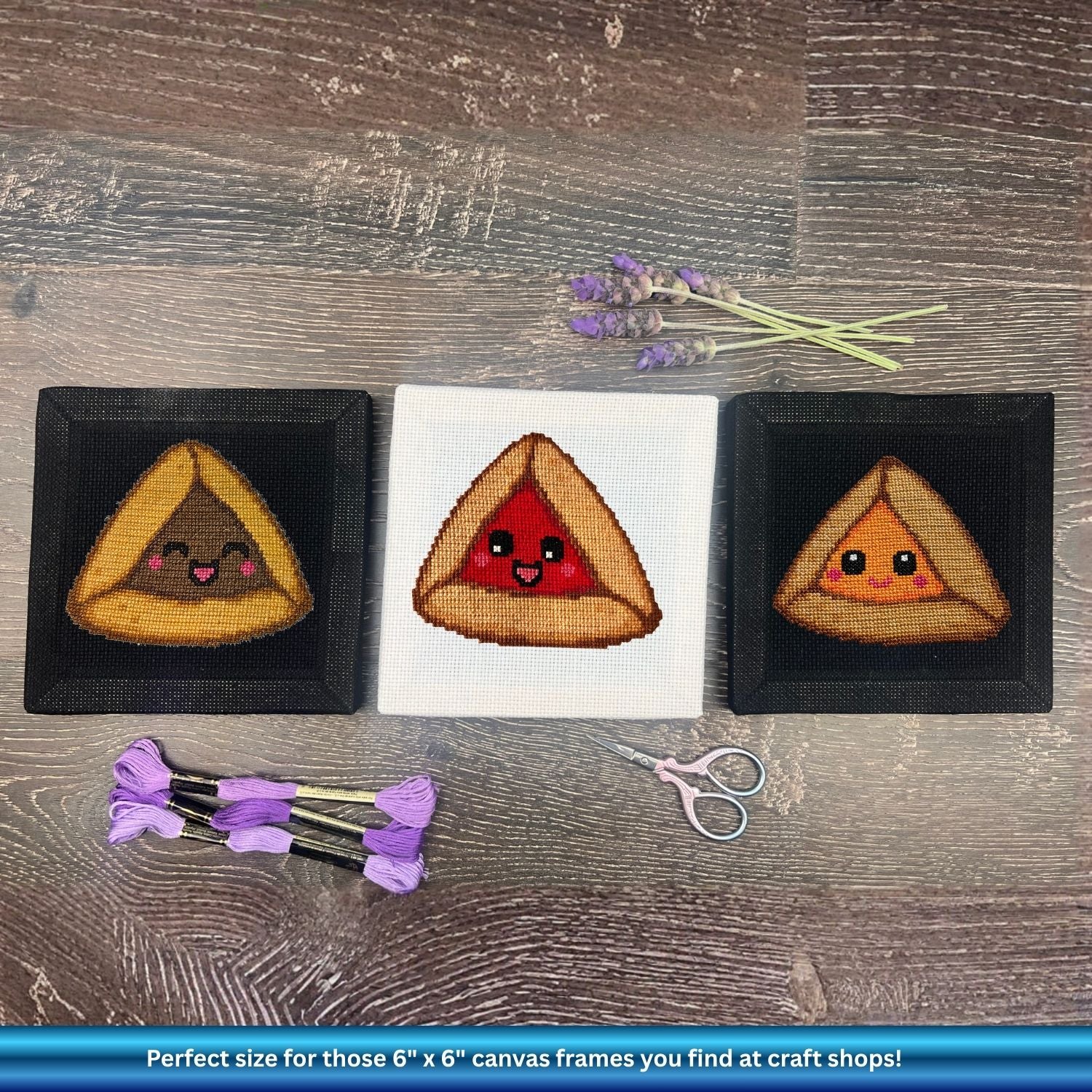 Three embroidered triangular hamantaschen with faces on a wooden surface with scissors and lavender.