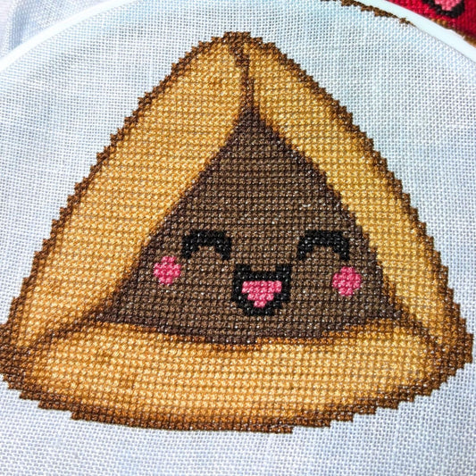 Cross-stitched design of a kawaii-style chocolate hamantaschen on 32 count linen.
