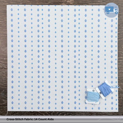 Cross-stitch fabric with blue pattern of Hamsa's on a wooden surface, featuring a bobbin of thread.