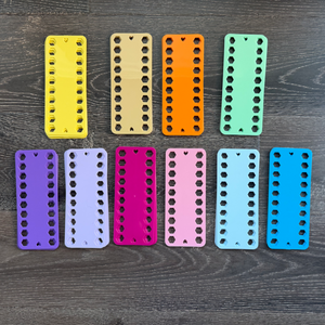 Ten colorful plastic embroidery floss organizers arranged in a row on a wooden surface.