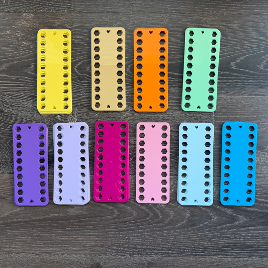 Ten colorful plastic embroidery floss organizers arranged in a row on a wooden surface.