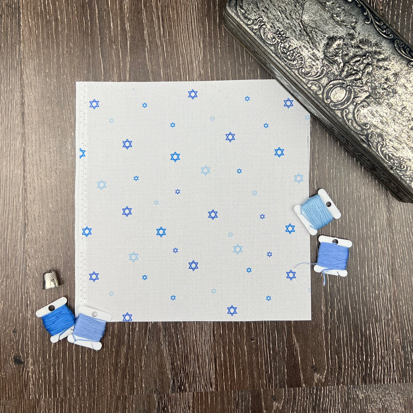 White Aida needlecraft fabric with blue stars of David in a repeating pattern.