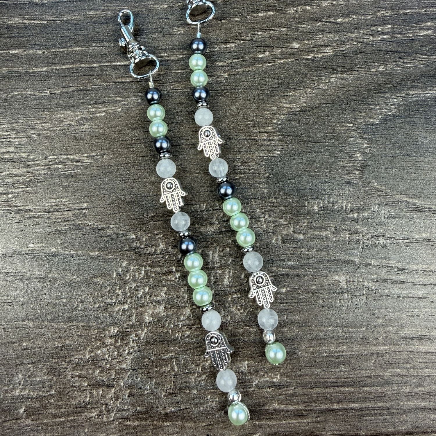 Pair of beaded zipper pulls with Hamsa hand charms on a wooden velvet background