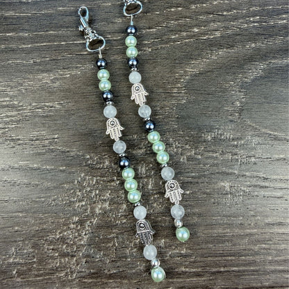 Pair of beaded zipper pulls with Hamsa hand charms on a wooden velvet background