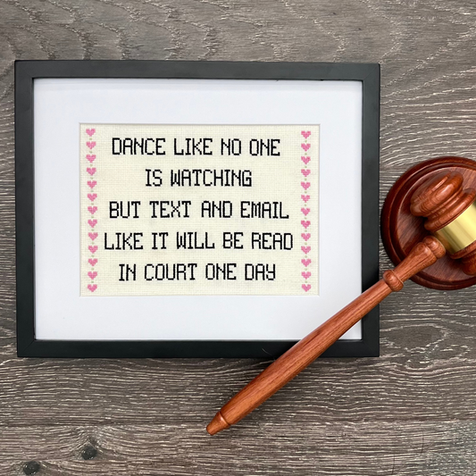 Framed cross-stitched quote with a gavel on a wooden surface