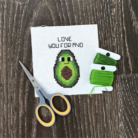Embroidery kit with a cross-stitch avocado design and text on a wooden surface