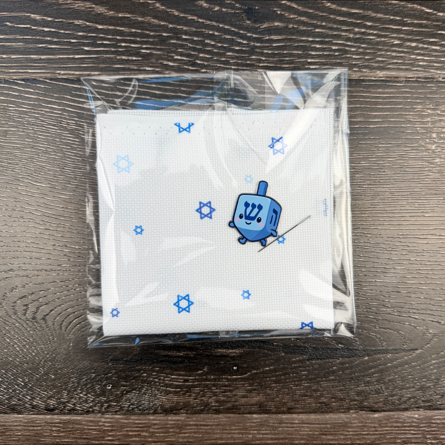 Hanukkah dreidel needle minder on top of Jewish Aida fabric on a wooden surface