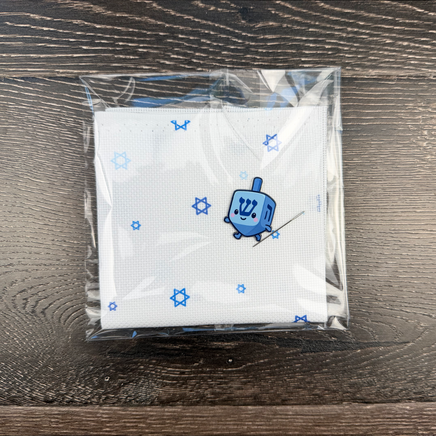 Hanukkah dreidel needle minder on top of Jewish Aida fabric on a wooden surface