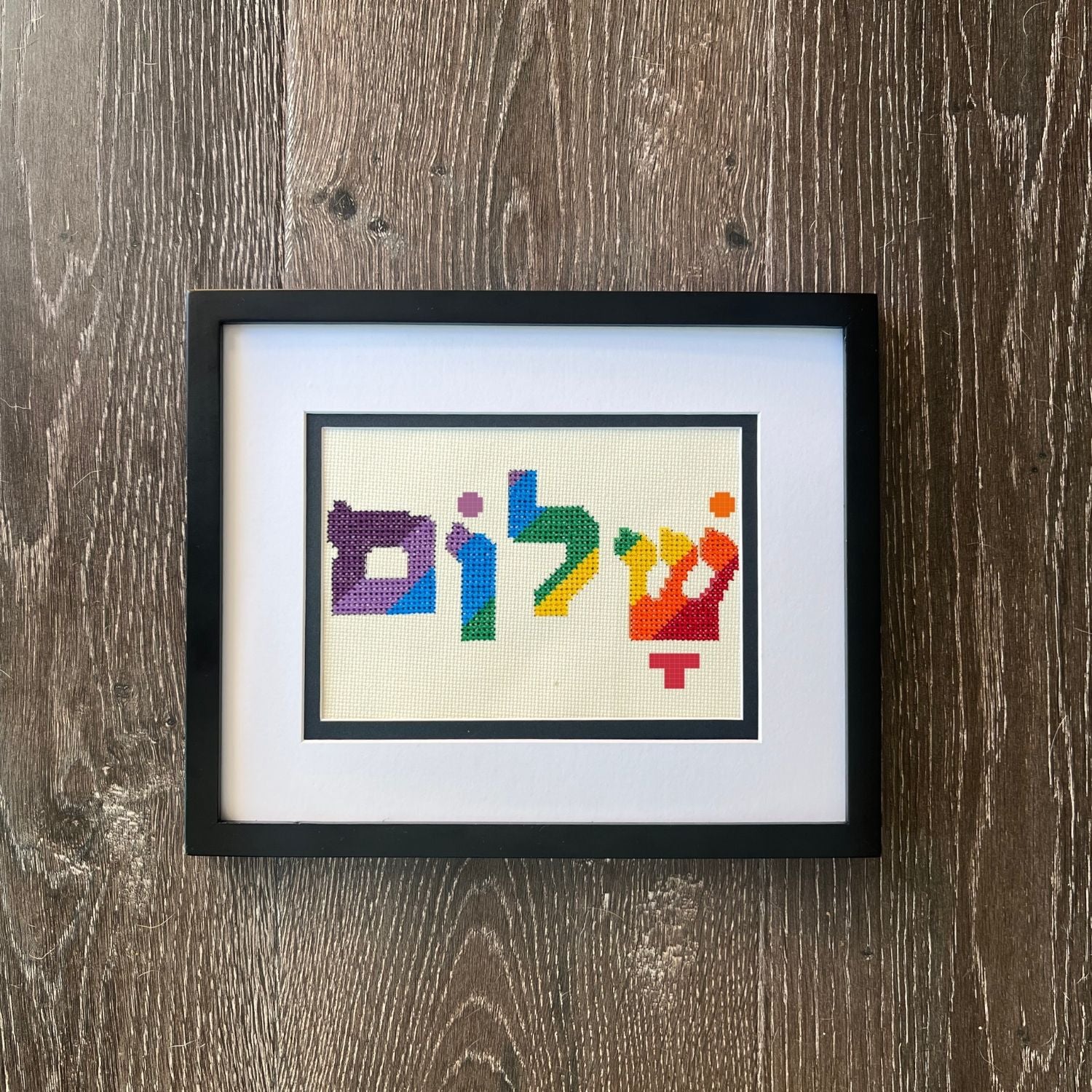 Embroidery hoop with colorful Hebrew letters on a wooden surface with blue fabric.