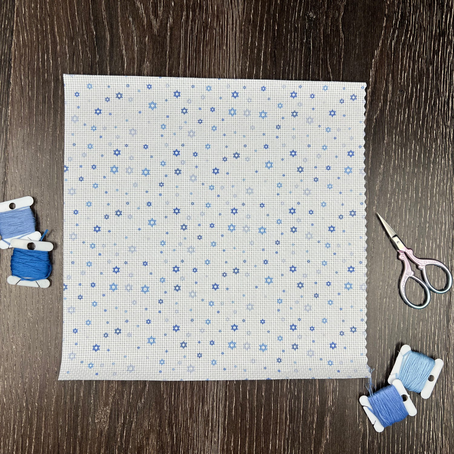 Fabric with blue stars of david pattern on a wooden surface with scissors and thread spools.