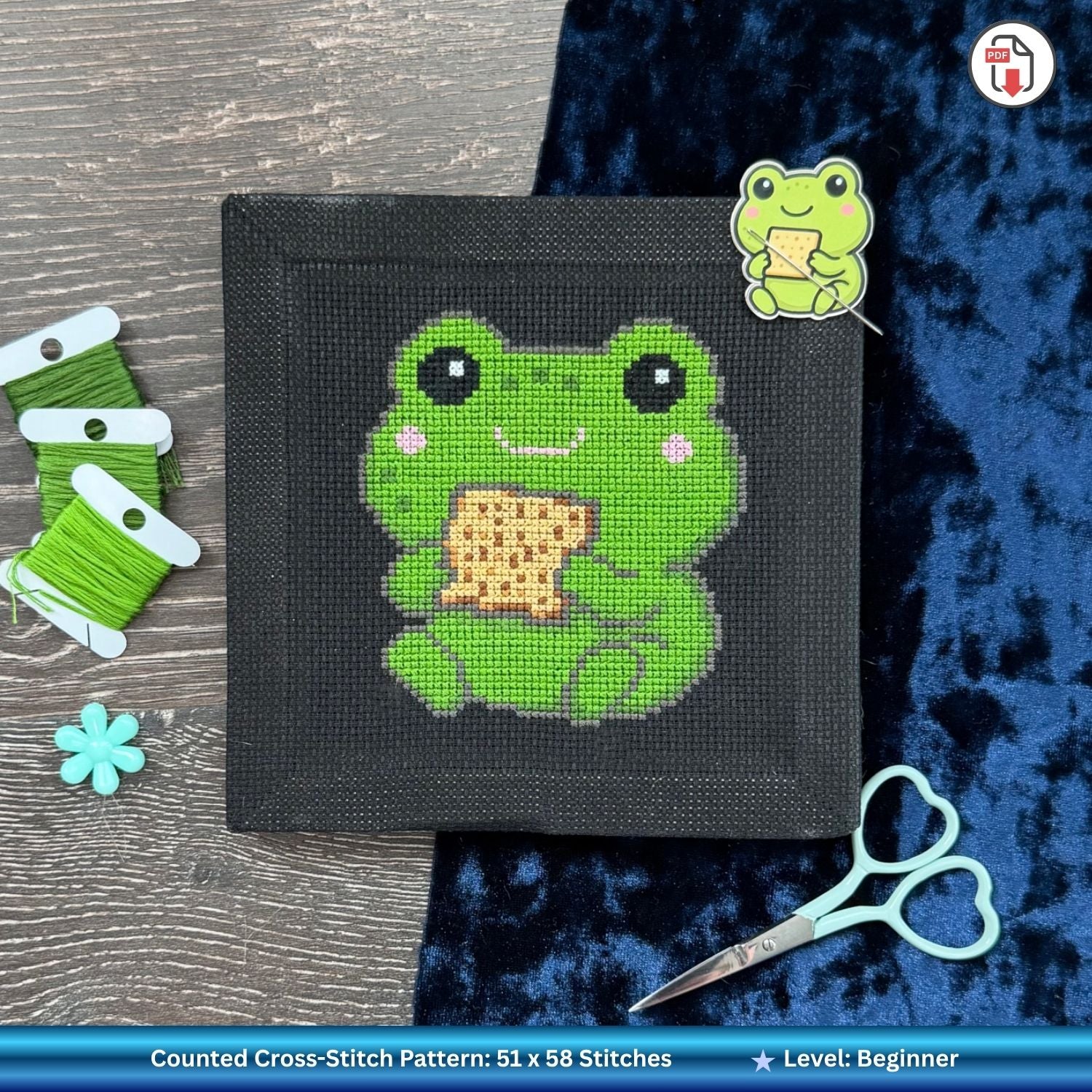 Finished cross-stitched Pesach frog design eating matzah with scissors and embroidery needle holder