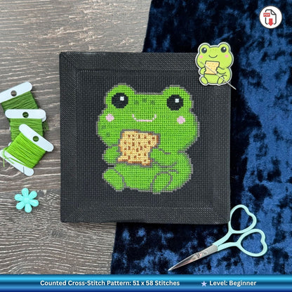 Finished cross-stitched Pesach frog design eating matzah with scissors and embroidery needle holder