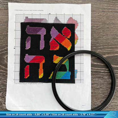 Cross-stitched design of the Hebrew word for Love (Ahava) with colorful letters Hebrew on black Aida, placed on a printed out pattern.