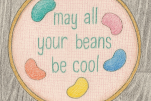 Embroidery hoop with colorful beans and text 'may all your beans be cool' on a wooden surface