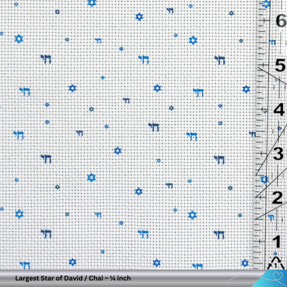 Cross-stitch fabric with blue Star of David and Chai patterns and a ruler for scale.
