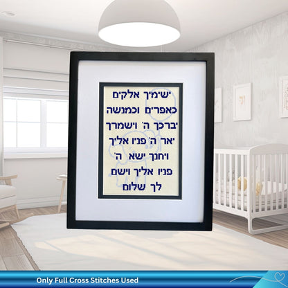 Framed cross-stitched artwork in a nursery with a crib and lamp.