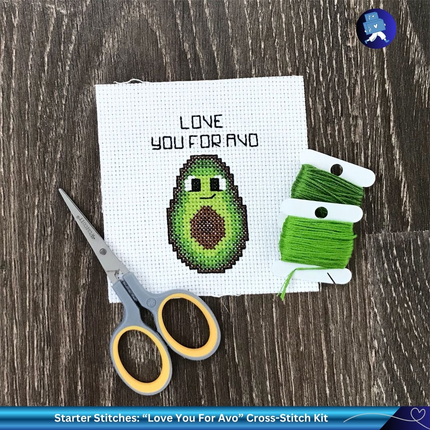 Cross-stitch kit with avocado design, scissors, and green thread on a wooden surface