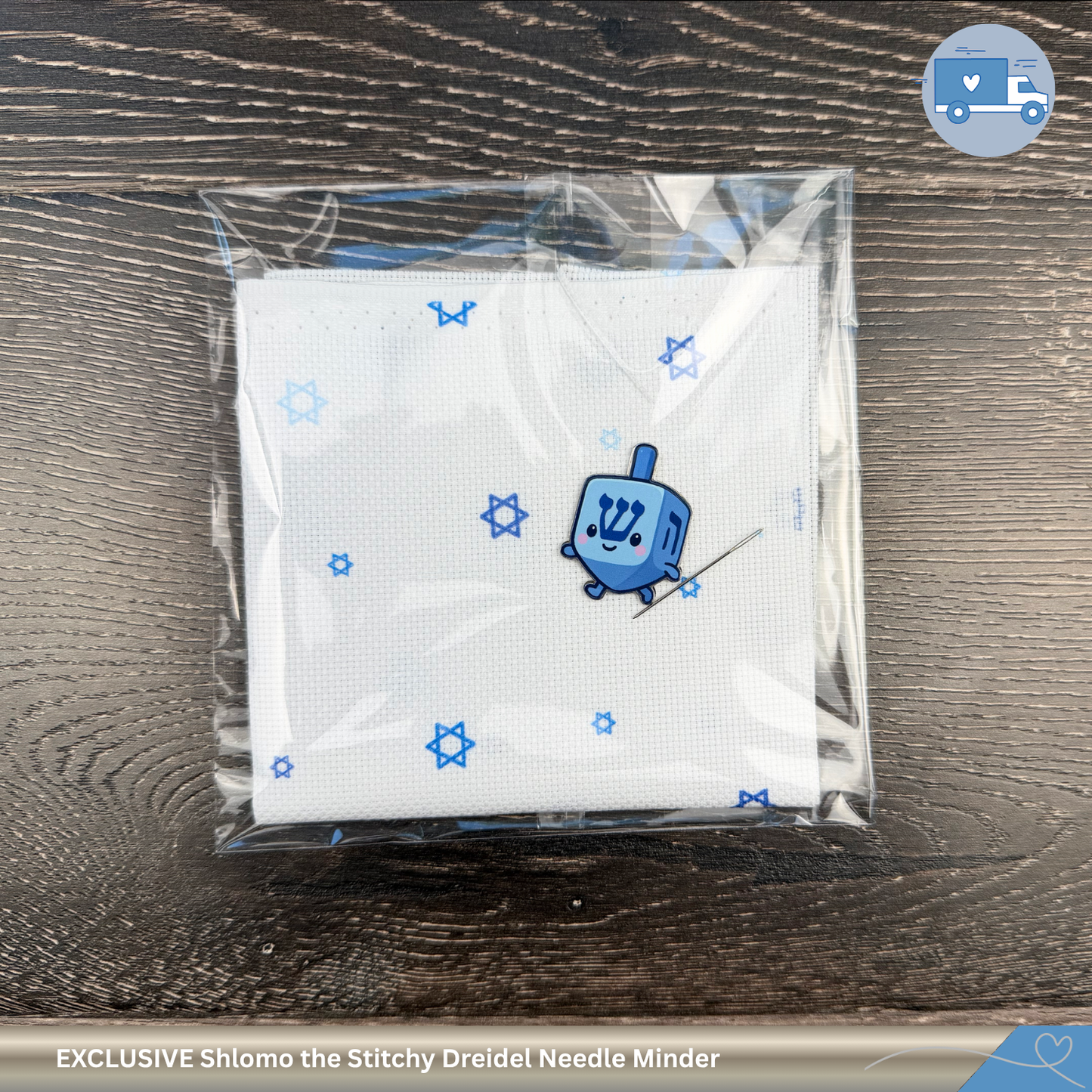 Blue dreidel needle minder on top of Star of David aida fabric on a wooden surface