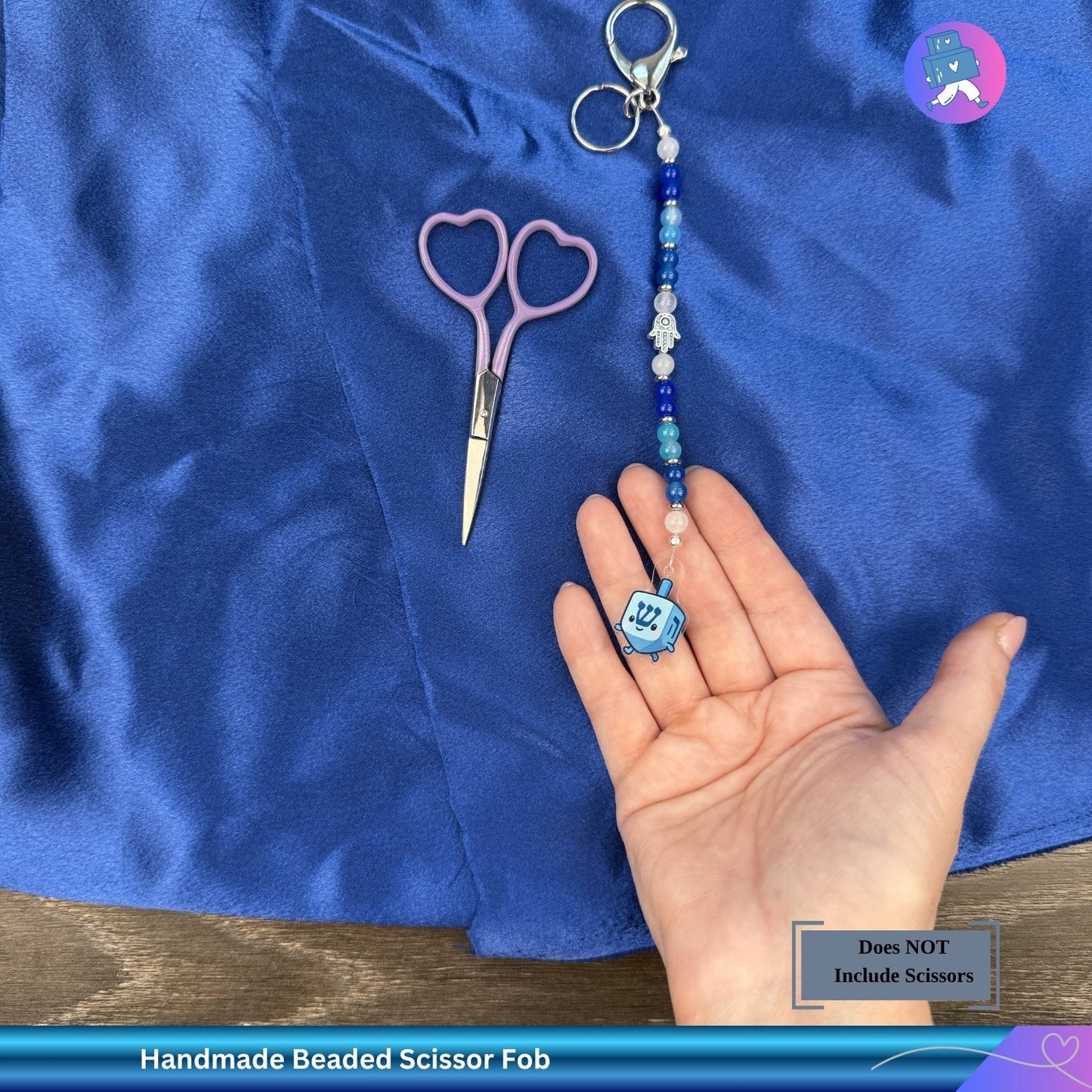 Handmade beaded scissor fob held in a hand with scissors and blue fabric in the background