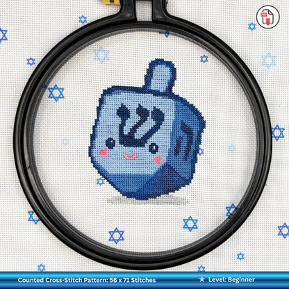 Cross-stitch pattern of a blue dreidel with a smiling face on a white background with Magen David patterns.
