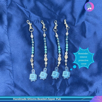 Set of handmade Shlomo beaded zipper pulls on a blue satin background