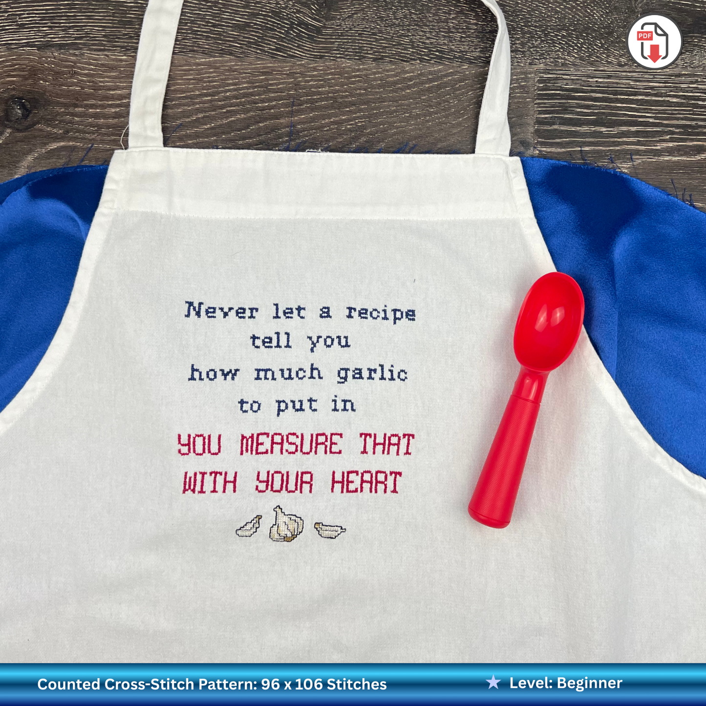 White apron with embroidered humorous text and red measuring spoon on a wooden surface