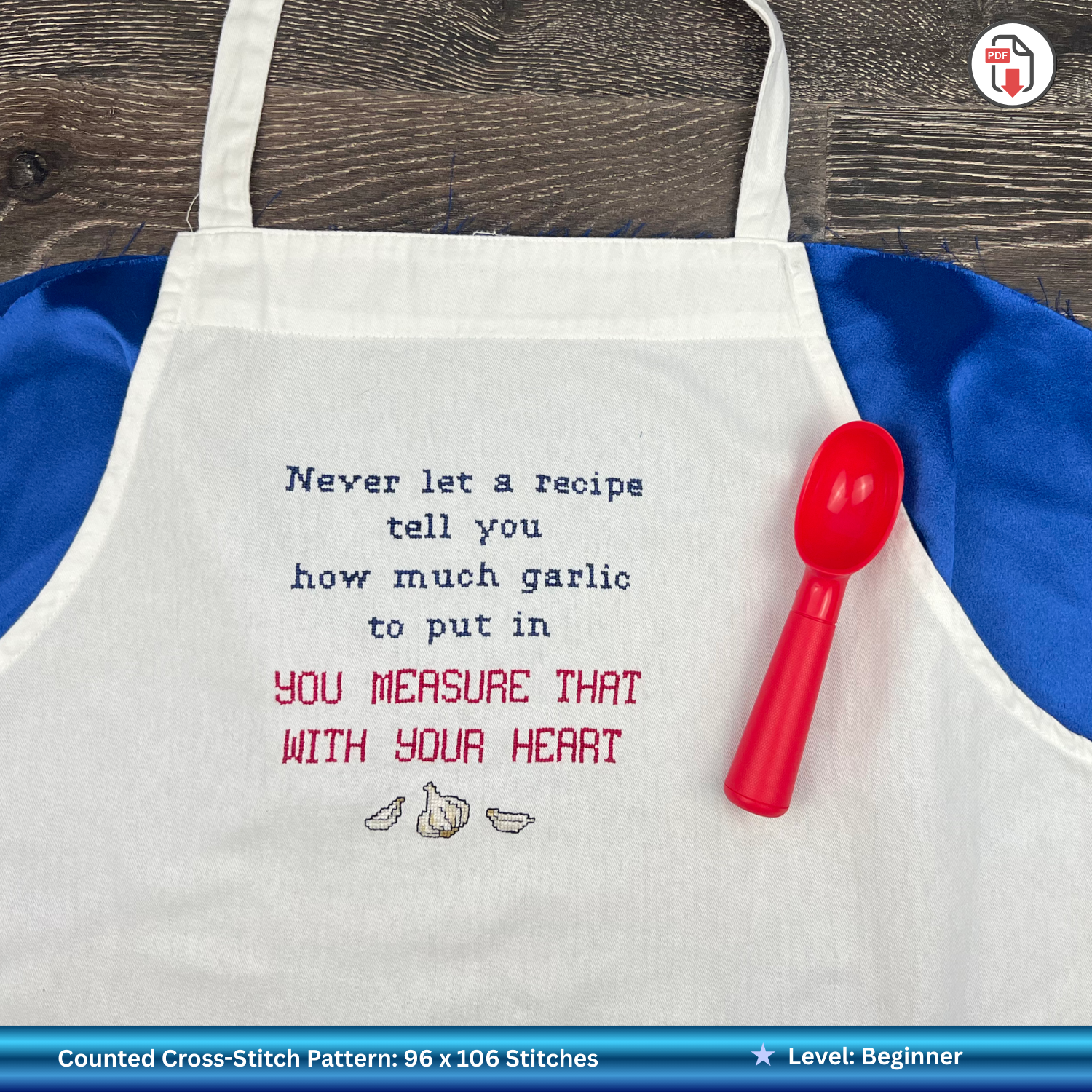 White apron with embroidered humorous text and red measuring spoon on a wooden surface