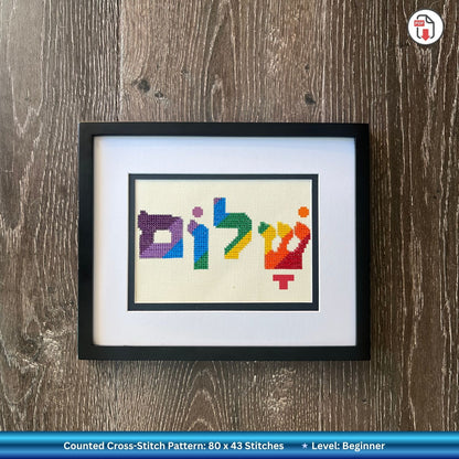 Embroidery hoop with Hebrew word for Shalom cross-stitched colorful letters on a wooden surface with blue fabric.