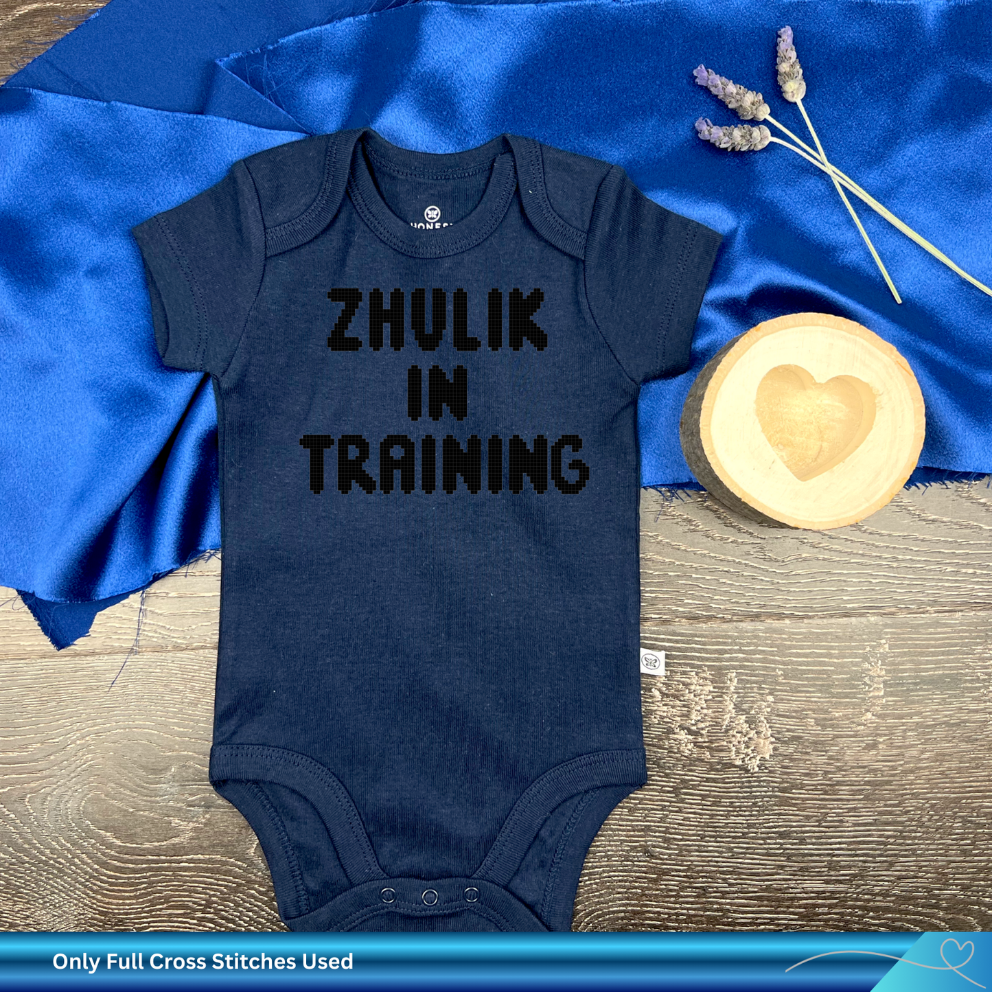 Navy blue baby onesie with 'ZHULIK IN TRAINING' text on a blue fabric background.