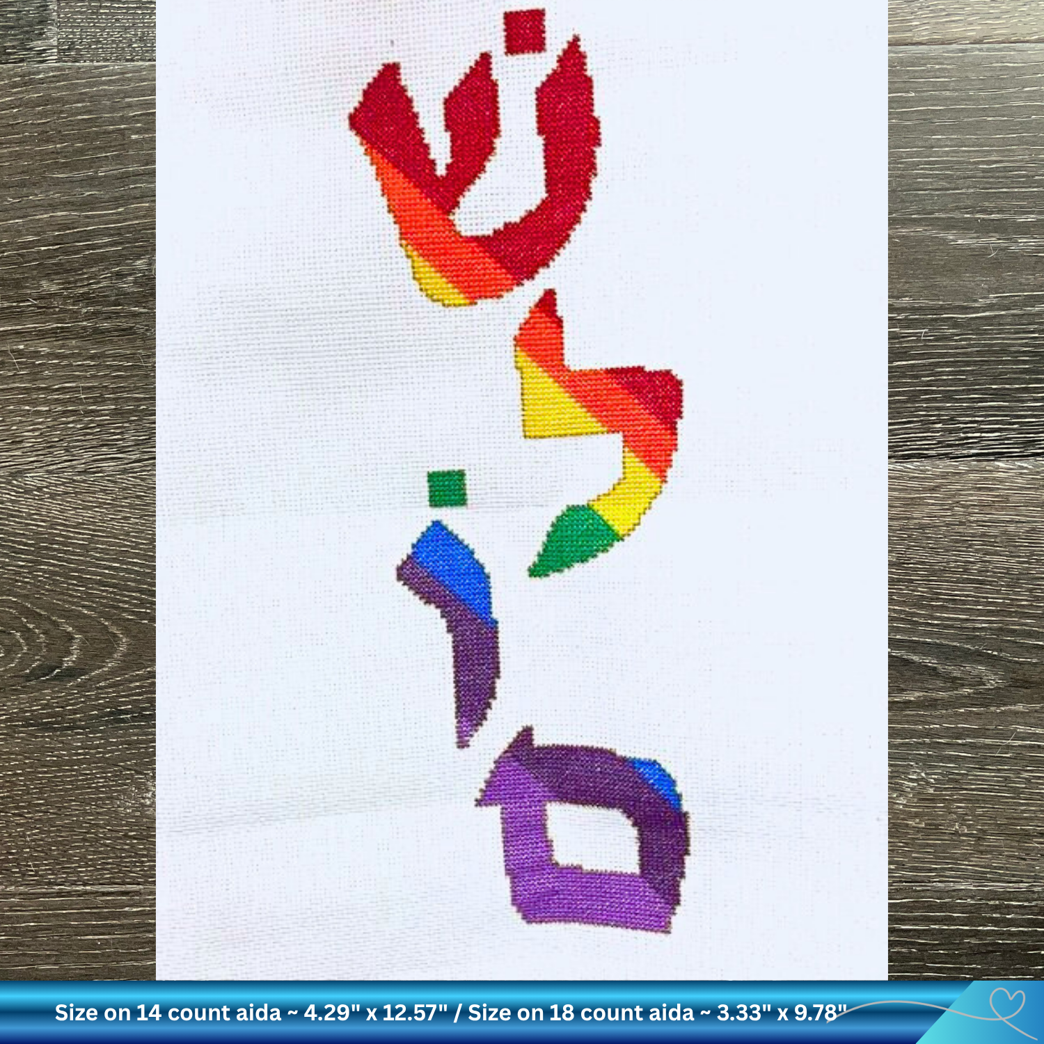 Colorful embroidered Shalom design on white Aida fabric with a wooden background