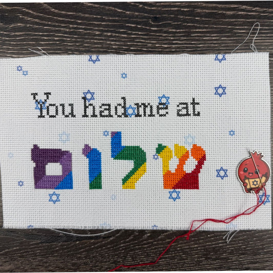 Cross-stitched project with colorful Hebrew letters and text on a wooden surface