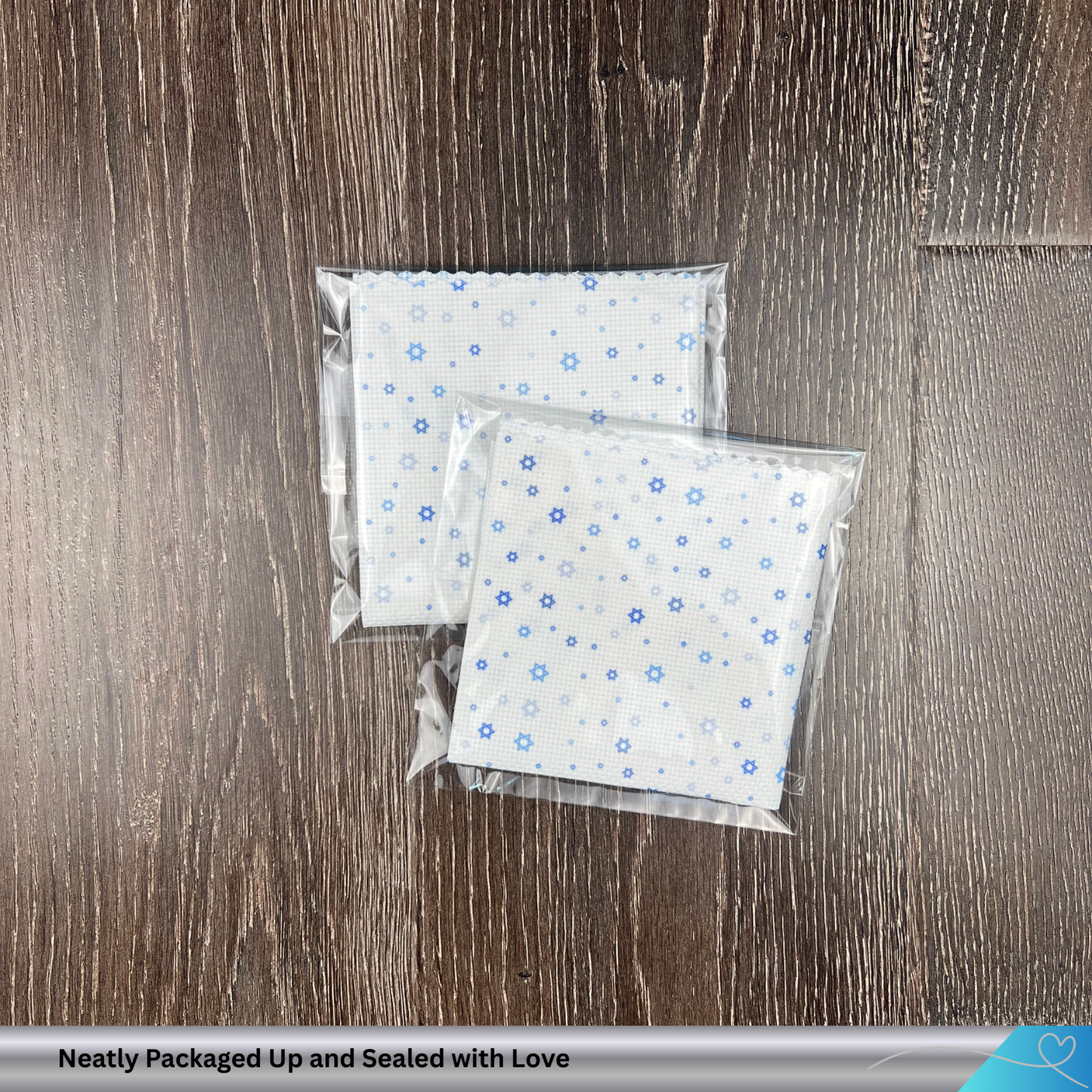 Two packages of white cross stitch fabric with blue Jewish star of david patterns on a wooden surface, labeled 'Neatly Packaged Up and Sealed with Love'.
