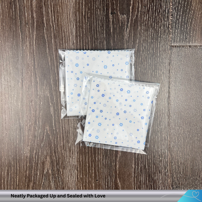 Two packages of white cross stitch fabric with blue Jewish star of david patterns on a wooden surface, labeled 'Neatly Packaged Up and Sealed with Love'.