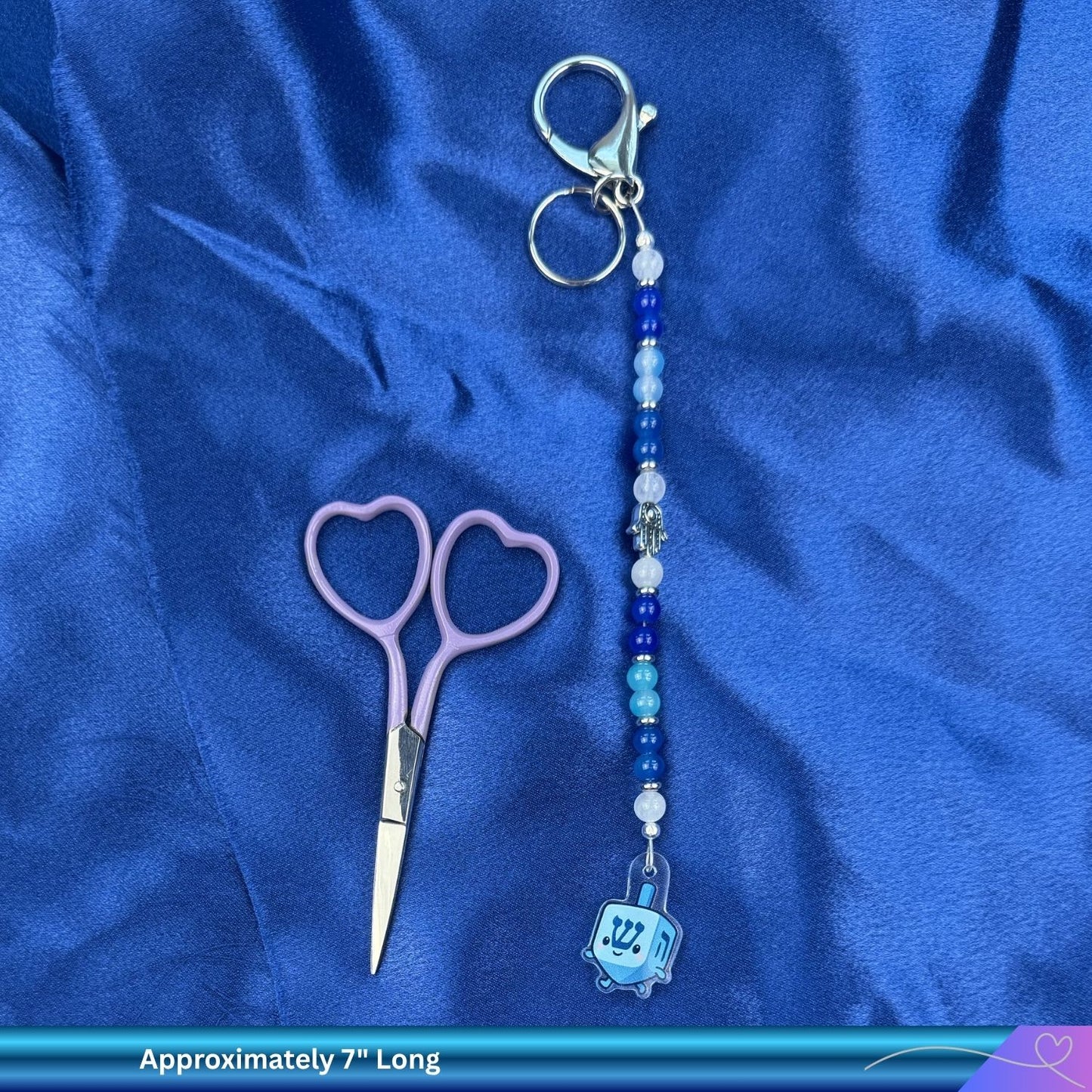 Scissors and a keychain with beads and a sweet dreidel charm on a blue fabric background