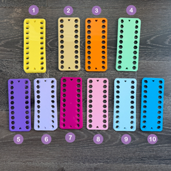 Ten colorful plastic embroidery thread organizers arranged in a row on a wooden surface.