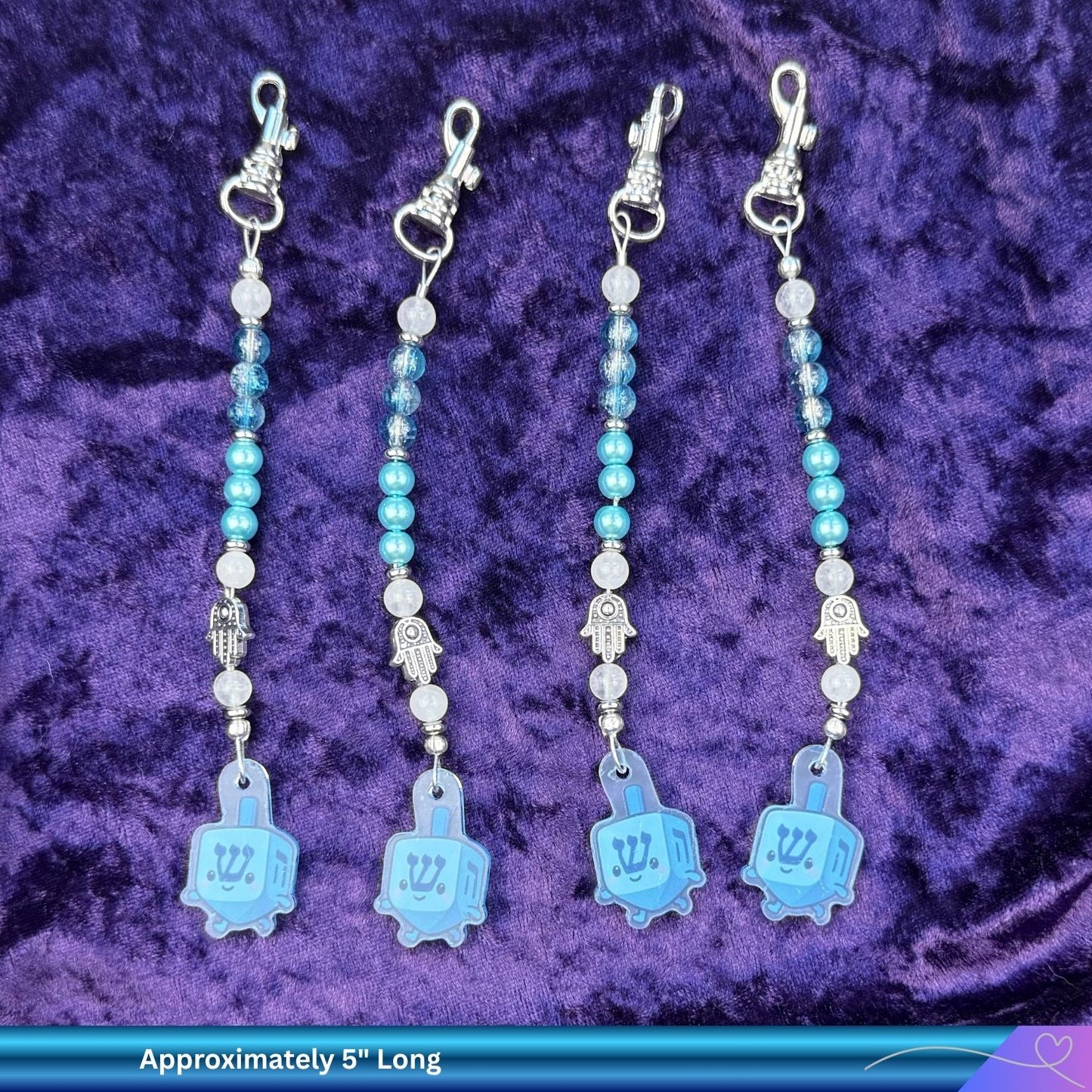 Four blue and silver Jewish zipper fobs with charms on a purple textured background