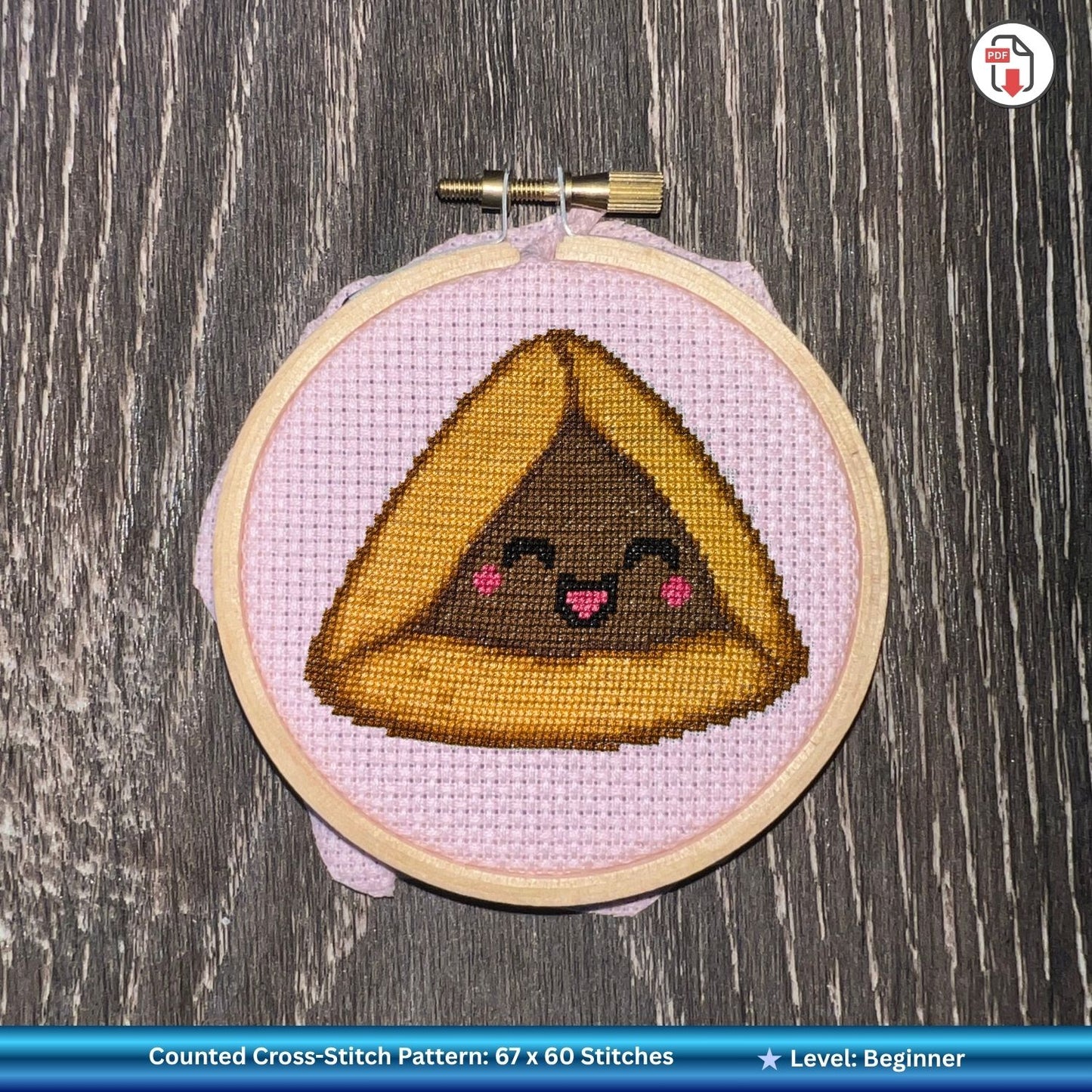 Cross-stitched hamantaschen with a face in an embroidery hoop on a wooden surface