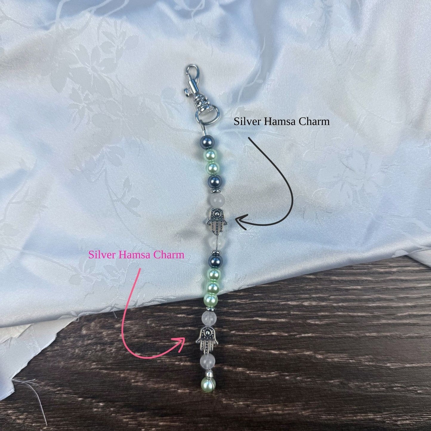 Four beaded keychains with blue dreidel charms and silver hamsa on a white fabric background.