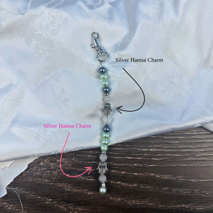Four beaded keychains with blue dreidel charms and silver hamsa on a white fabric background.