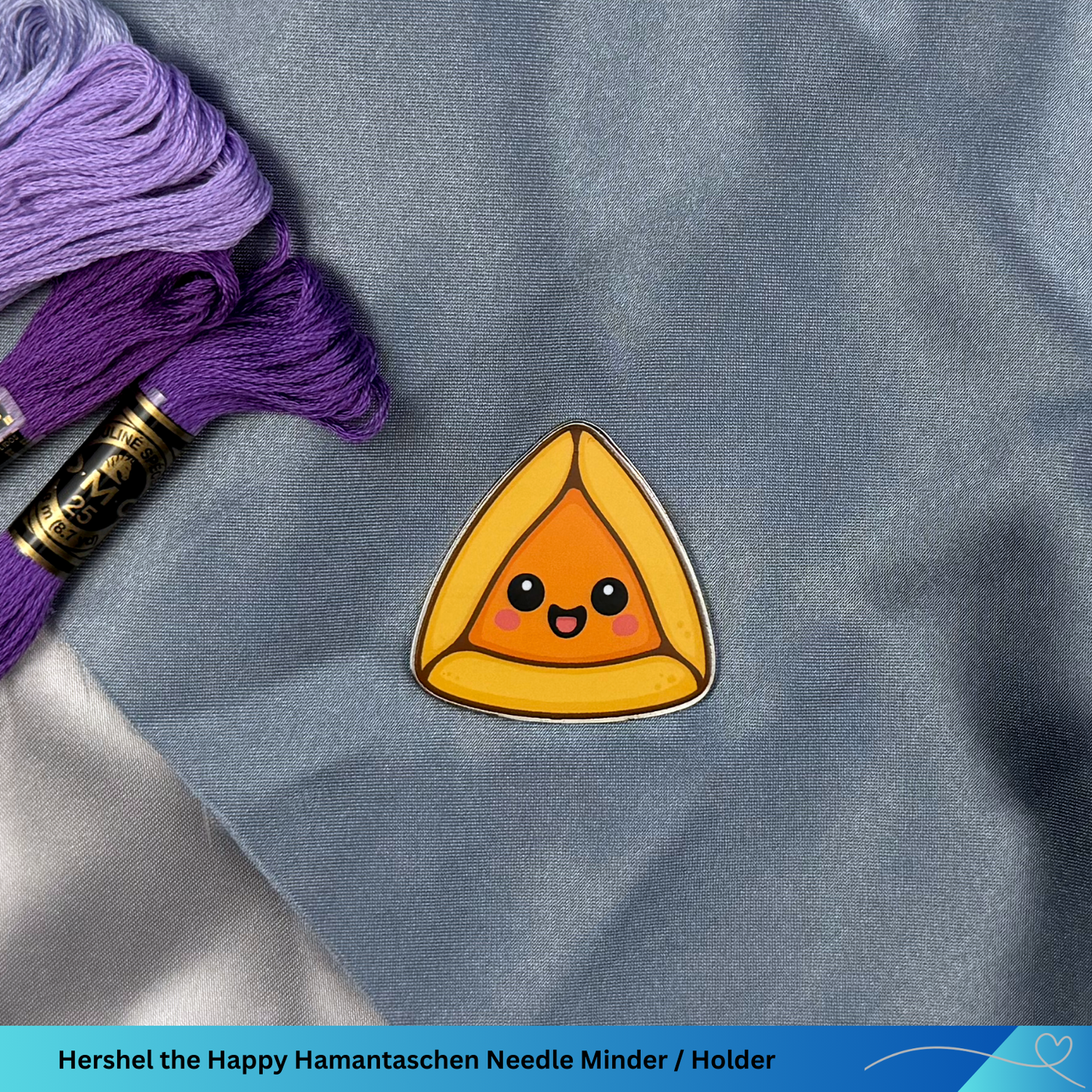 Happy Hamantaschen needle minder on a gray fabric background with purple thread.