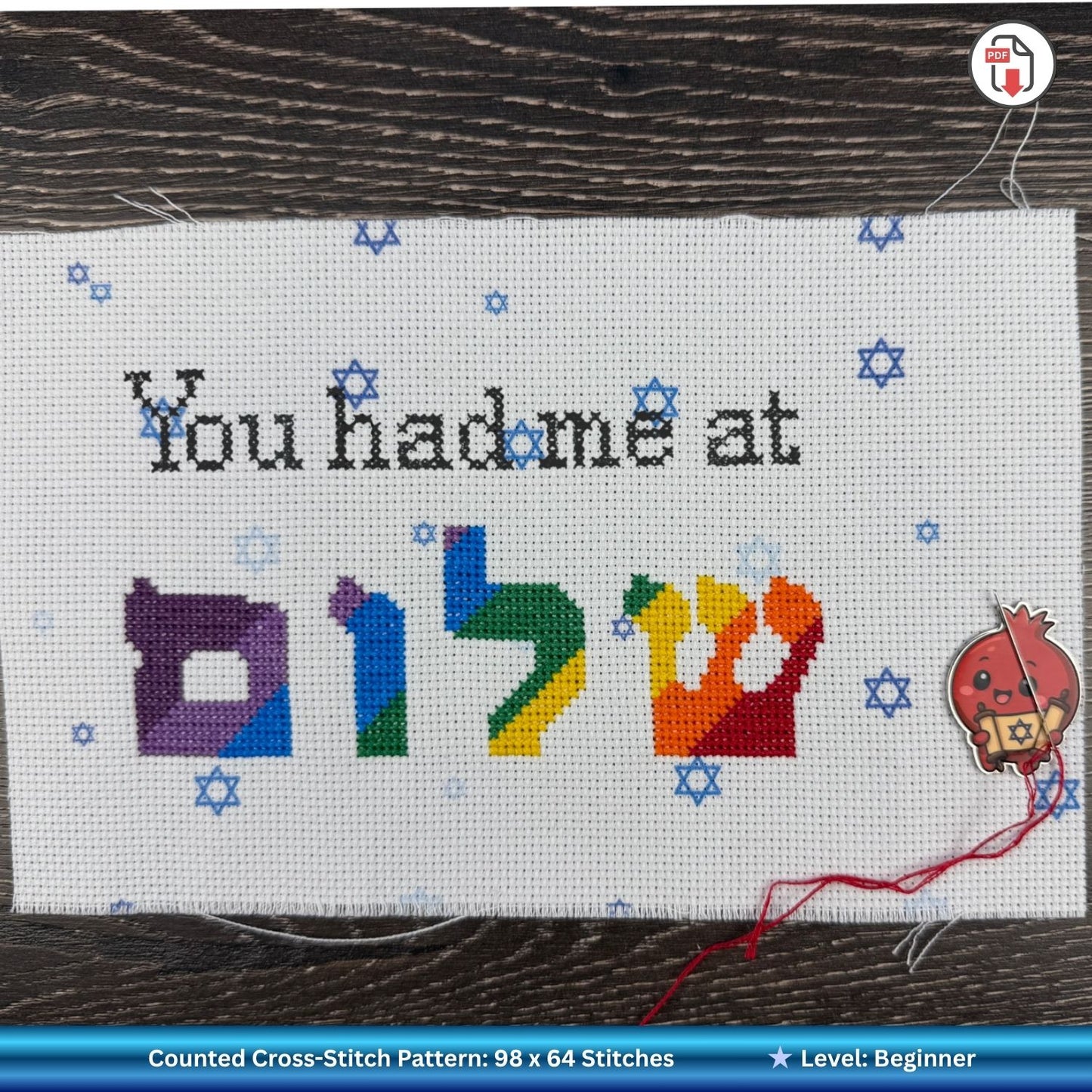 Cross-stitch pattern with colorful Hebrew letters and text on a wooden surface