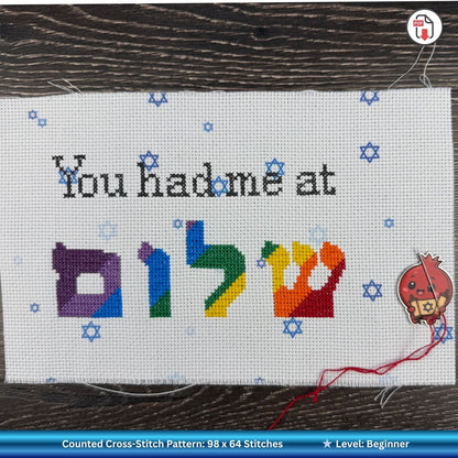 Cross-stitch pattern with colorful Hebrew letters and text on a wooden surface