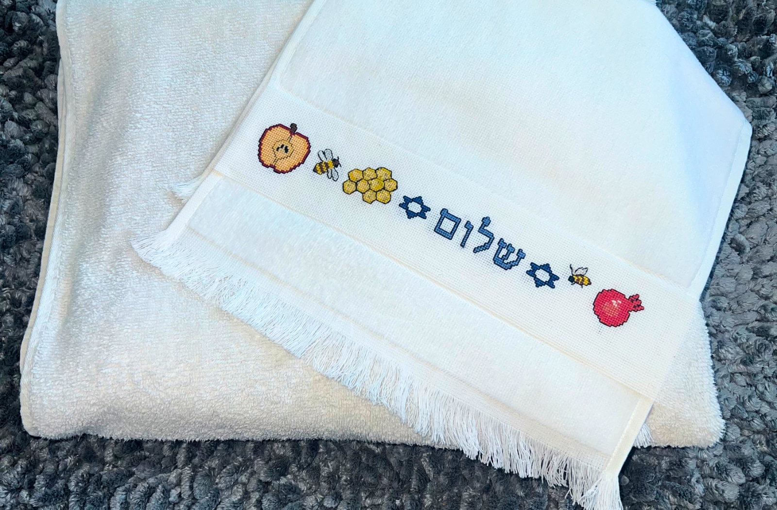 Folded white towel with embroidered Rosh Hashanah Jewish New Years designs on a textured surface